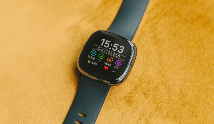 A Fitbit smartwatch displaying health metrics on a yellow background