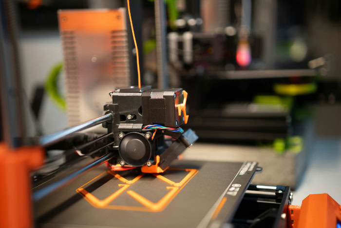 Close up of 3D printer extruding orange filament