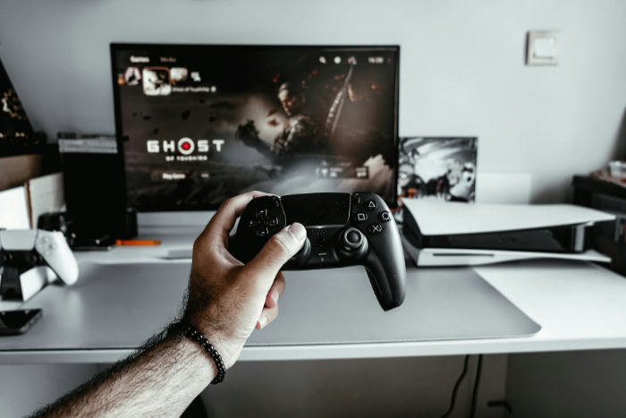 Hand holding PlayStation controller with Ghost of Tsushima on screen