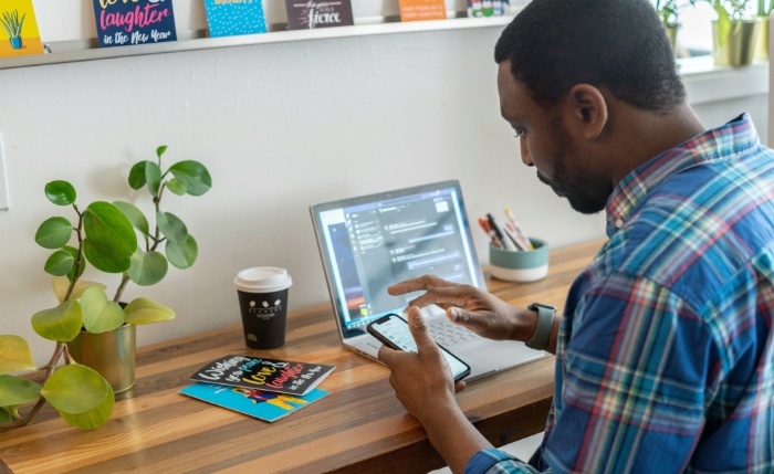 Man using smartphone while working on laptop in a home office