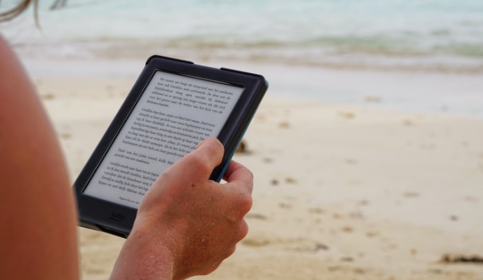Person reading a Kindle on a beach near the water