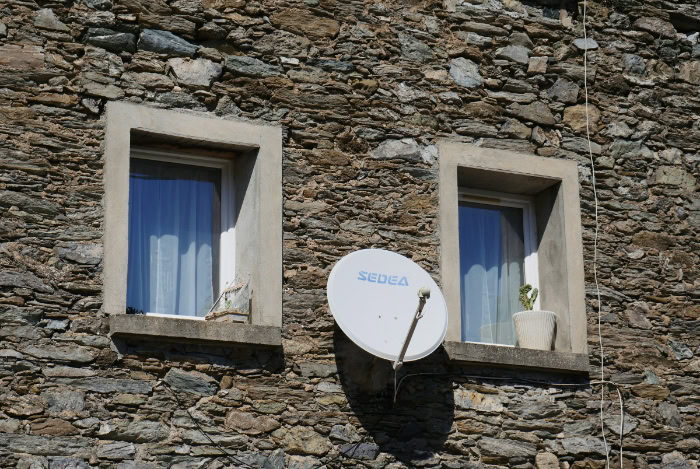 Satellite TV dish attached to stone house wall