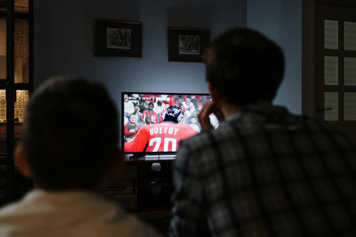 Two people watching a live hockey game on TV